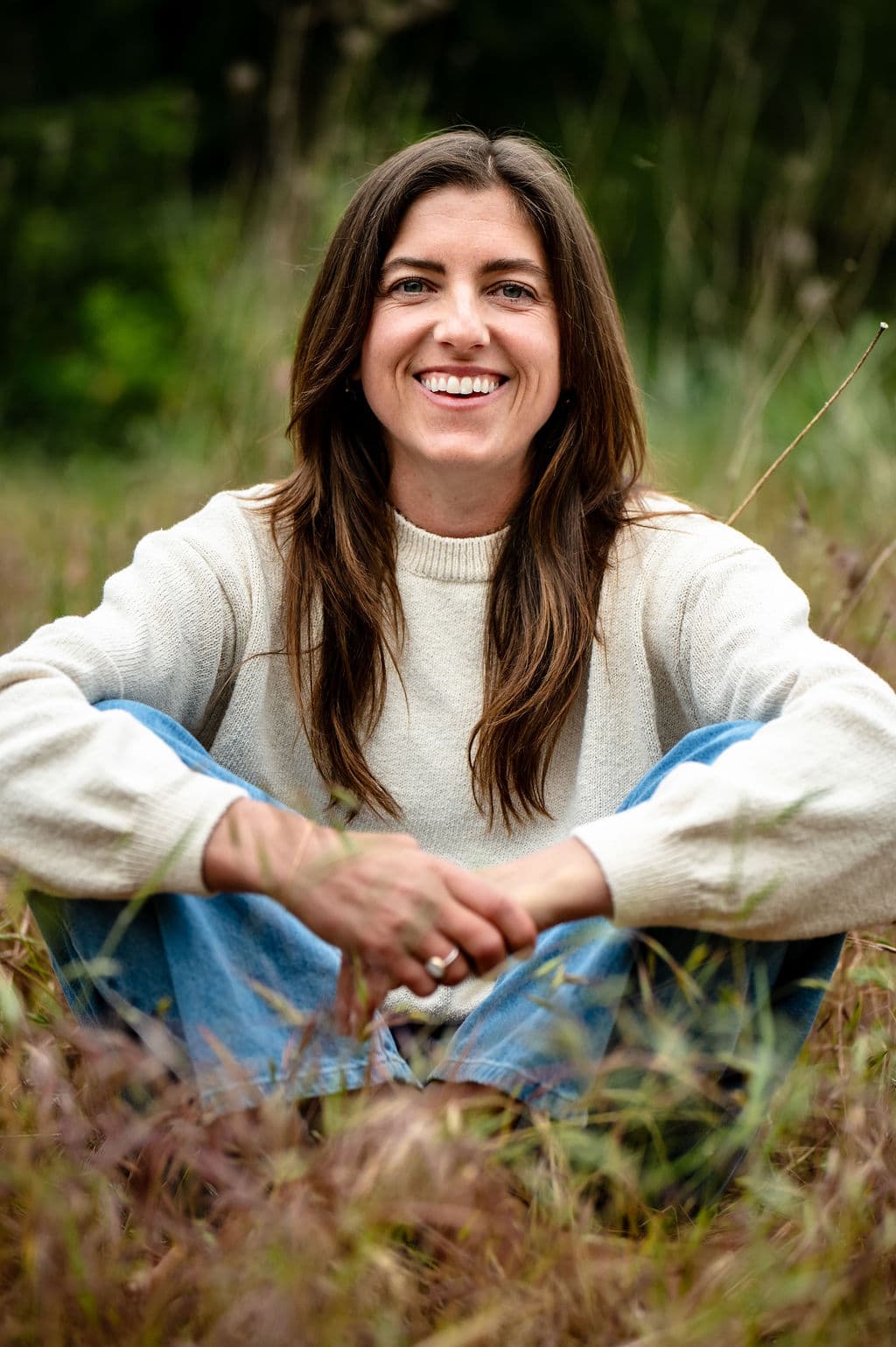 Chrystal smiling while seated in a grassy meadow.