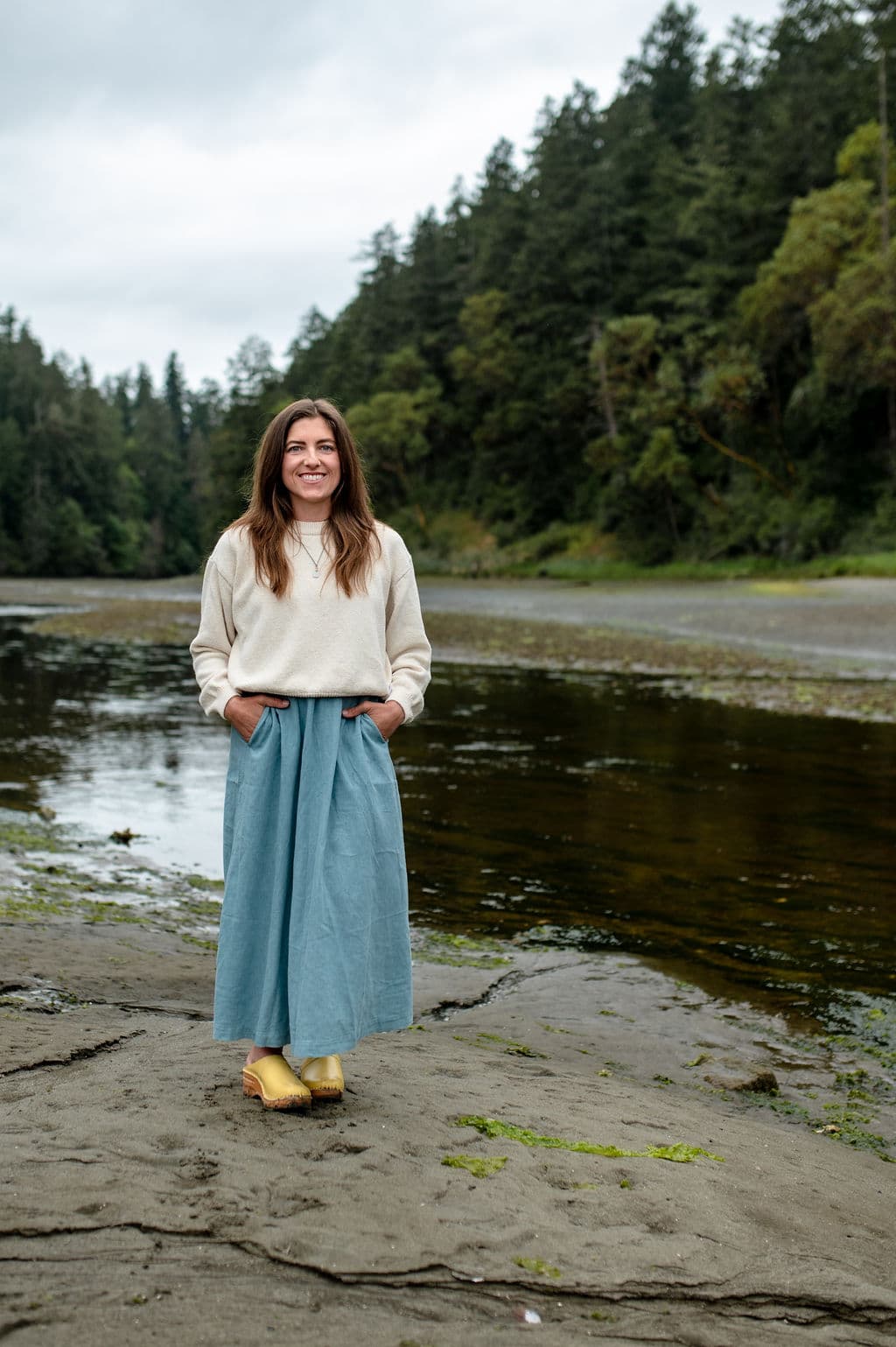Chrystal standing beside a river framed by evergreen forest.